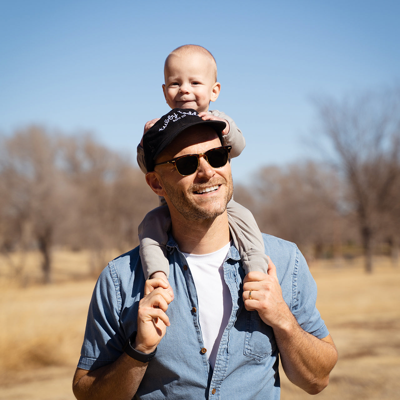 A dad wearing a mama hat and riding a baby on his shoulders.
